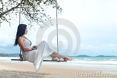 Summer Vacations. Lifestyle women relaxing and enjoying swing on the sand beach, fashion stunning women with white dress on the tr Stock Photo