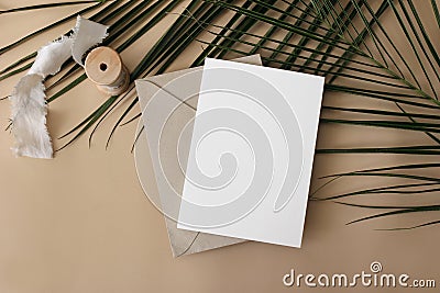 Summer wedding stationery mock-up, desk scene. Blank greeting card, envelope, ribbon and green palm leaves on beige Stock Photo