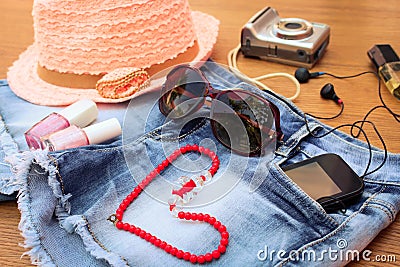 Summer women's accessories: red sunglasses, beads, denim shorts, mobile phone, headphones, a sun hat, camera, nail polish Stock Photo