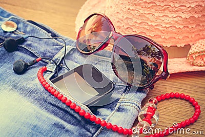 Summer women's accessories: red sunglasses, beads, denim shorts, mobile phone, headphones, a sun hat. Toned image Stock Photo
