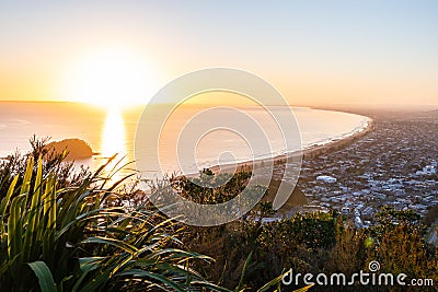 From the summit of Mount Maunganui at daybreak golden glow of rising sun, distant horizon and long leading coastline of Bay of Stock Photo