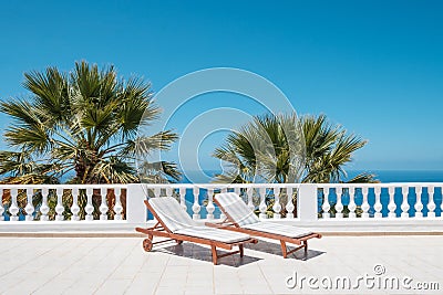 Two sun beds on villa terrace with ocean and palm tree background Stock Photo