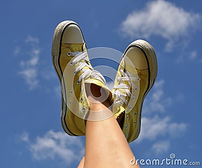 Sun burnt woman's feet in bright yellow sneakers against the deep blue sky background Stock Photo