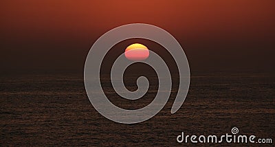 Sun disappearing below horizon at sunset on the ocean Stock Photo