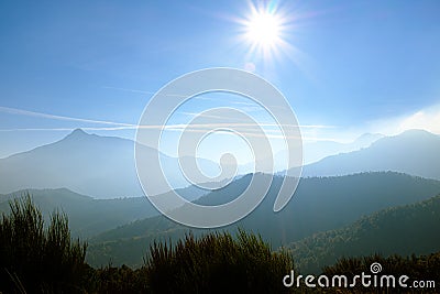 Sun flare shining on a solid blue sky on a foggy mountain landscape Stock Photo