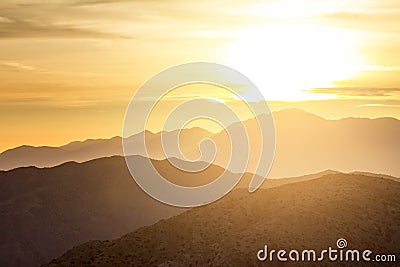 Sun glowing behind clouds and mountains in a desert landscape sc Stock Photo