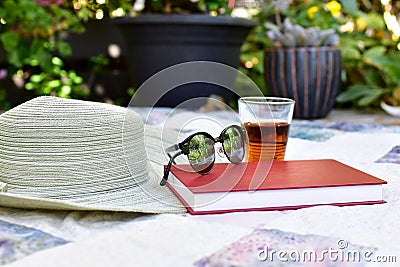 Sun hat and glasses with cold glass of iced tea on picnic blanket for relaxing afternoon reading Stock Photo