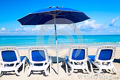 Sun loungers near blue umbrella on the sandy beach by the sea and sky. Vacation background. Idyllic beach landscape Stock Photo