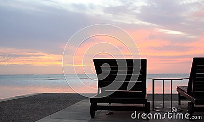 Sun lounges overlooking infinity pool and beach at sunset in a tropical resort Stock Photo