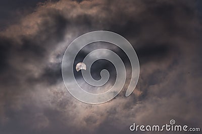 The sun during a partial solar eclipse with dark clouds . Stock Photo