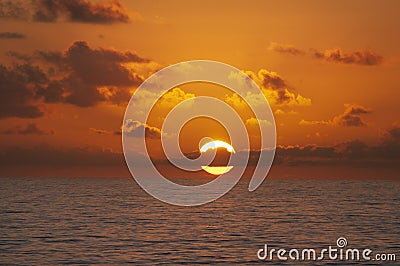 The sun rising with clouds going through center on ocean. Stock Photo