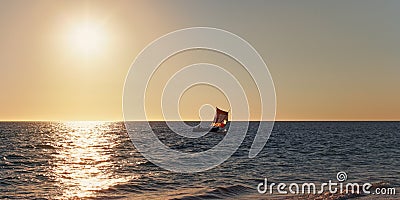 Sun setting down to calm sea, small sail piroga boat with silhouette of unknown man in distance Stock Photo