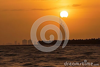 the sun is setting over a city on the horizon of the ocean with a boat in the foreground and a buliding in the distance Stock Photo