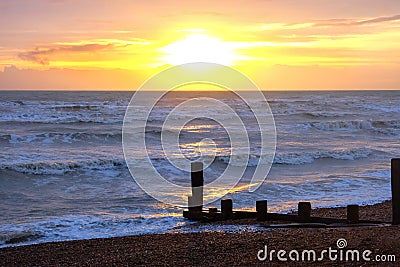 Sun setting over a sea with waves breaking and a wooden sea break, Brighton, Uk Stock Photo