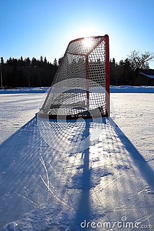 Sun silhouetting a empty hockey net on a frozen pond Stock Photo