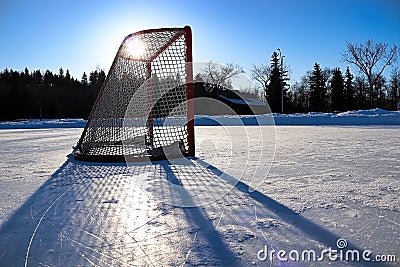 Sun silhouetting a empty hockey net on a frozen pond Stock Photo