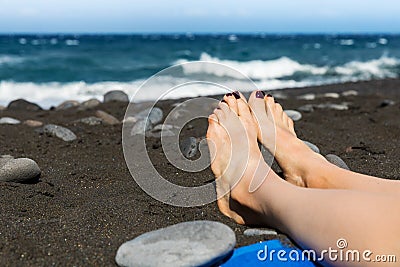 Sunbathing - woman feet on black sand beach Stock Photo