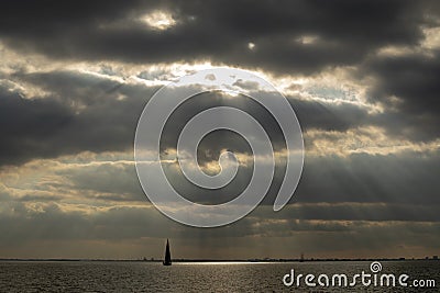 Sunbeams breaking through cloud cover, a sailboat sailing on a lake near Amsterdam. Stock Photo