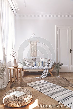 Sunbeams on a wicker ottoman and herringbone floor of a beige living room interior with a wooden sofa and cushions Stock Photo