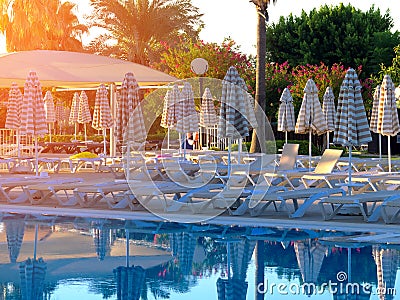 Sunbeds and folded umbrellas next to swimming pool Stock Photo