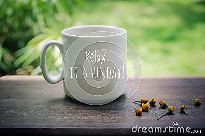 Sunday mug of coffee concept. Morning white coffee with text on it - Relax. It is Sunday, and yellow little flowers arrangement. Stock Photo