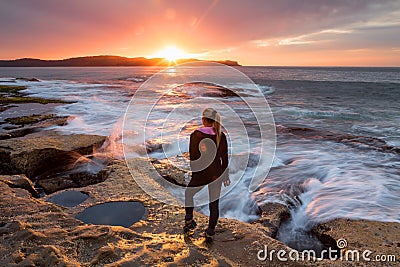 Sunflare kissing the shoulder of a woman watching sunrise by the ocean Stock Photo