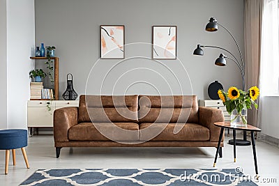 Sunflowers on wooden table next to leather sofa in living room interior with posters. Real photo Stock Photo