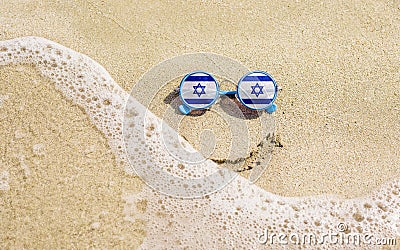 Sunglasses with flag of Israel on a sandy beach. Nearby is a sea lightning and a painted smile. Stock Photo