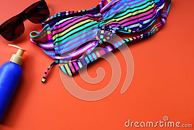 Sunglasses, sunscreen bottle, colored female swimsuit on an orange background with space for text. Stock Photo