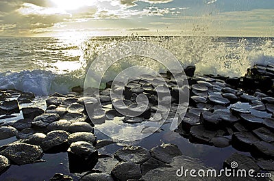 Sunlight highlighting waves crashing onto the hexagonal Basalt slabs of Giants Causeway Stock Photo