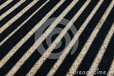 Sunlight shines through wooden fence and makes geometric stripes shadows on the ground. Shadows of wooden fence on the Stock Photo