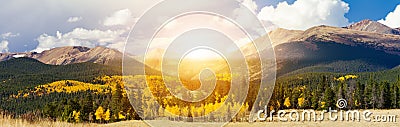 Sunlight shining over high mountain peaks and golden aspen trees in a panoramic Colorado landscape Stock Photo