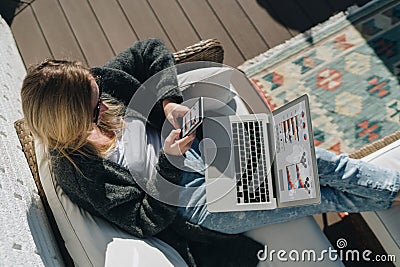 Sunny day. View from above. Young businesswoman is sitting on white couch, using laptop and smartphone with graphs Stock Photo