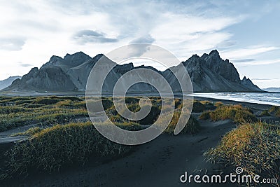 Sunny landscape of Iceland. Gorgeous view on Stokksnes cape and Vestrahorn Mountain with black sand with grass on Stock Photo