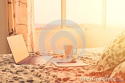 Sunny morning in modern apartment - open laptop on bed opposite window, next to cup of coffee and notebook. Stock Photo
