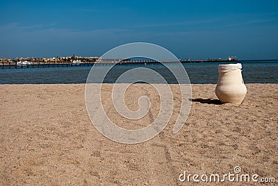 Sunny sand beach with jug and two tracks. Ceramic pot in sand on beach. Blue ocean and white jug on beach Stock Photo