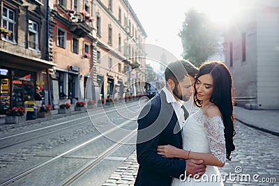 Sunny sensitive wedding portrait. Tenderly hugging beautiful couple of newlyweds in the town street. Stock Photo