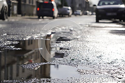 Sunny street after the rain. reflection, glare of the sun in puddles and wet asphalt, asphalt with holes in the city or village. Stock Photo