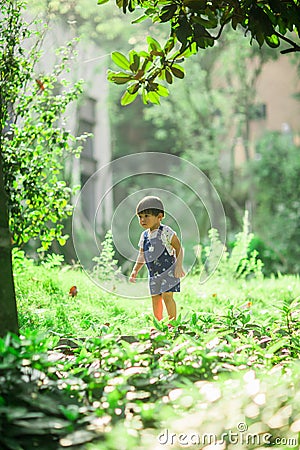 A lively little boy in blue overalls stands among the bushes in the park Stock Photo