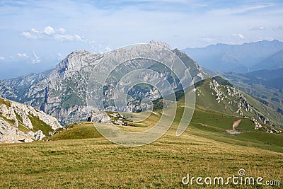 WALLPAPER sunny summer day in the mointains Green fields in front of a great mountain peak Massive rocks with blue sky and clouds Stock Photo