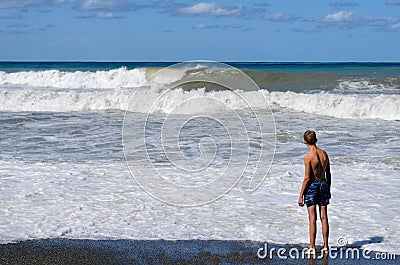 On a Sunny summer day, a teenager stands on the beach and watches the waves Stock Photo