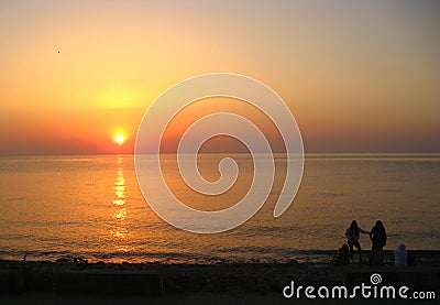 Sunrise. A group of young girls on a sea beach enjoys a beautiful sunrise scene. Stock Photo