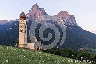 Sunrise landscapes of Church St. Valentin on grassy hilltop with view of rugged peaks of Mountain Schlern with alpenglow in backgr Stock Photo