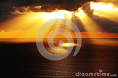 Golden sunlight through dark clouds over ocean Stock Photo