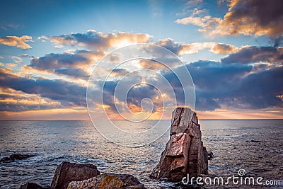 Sunrise over a rocky beach. Colorful clouds reflecting in the sea Stock Photo