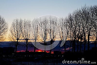 Sunrise over small town. Fiery dawn in the dark sky, horizontal photo. Silhouettes of trees, cars and industrial buildings Stock Photo