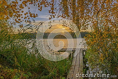 Sunrise over wooden pier on the lake. Wooden footbridge on the lake in the sunrise. A beautiful sunrise over lake greets the morni Stock Photo