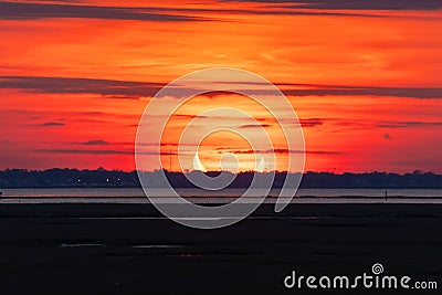 Sunrise during a partial solar eclipse, with a crescent shaped sun on the horizon over water. Stock Photo