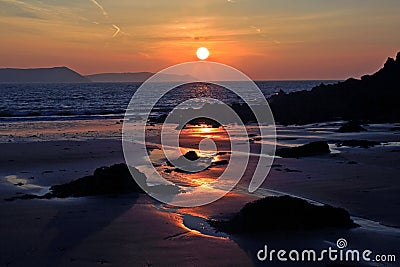 Sunrise reflected in the wet sand and rocks of Freshwater East beach Stock Photo