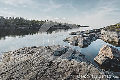 Sunrise on a rocky shore. Still water. Pine forest in the background Stock Photo